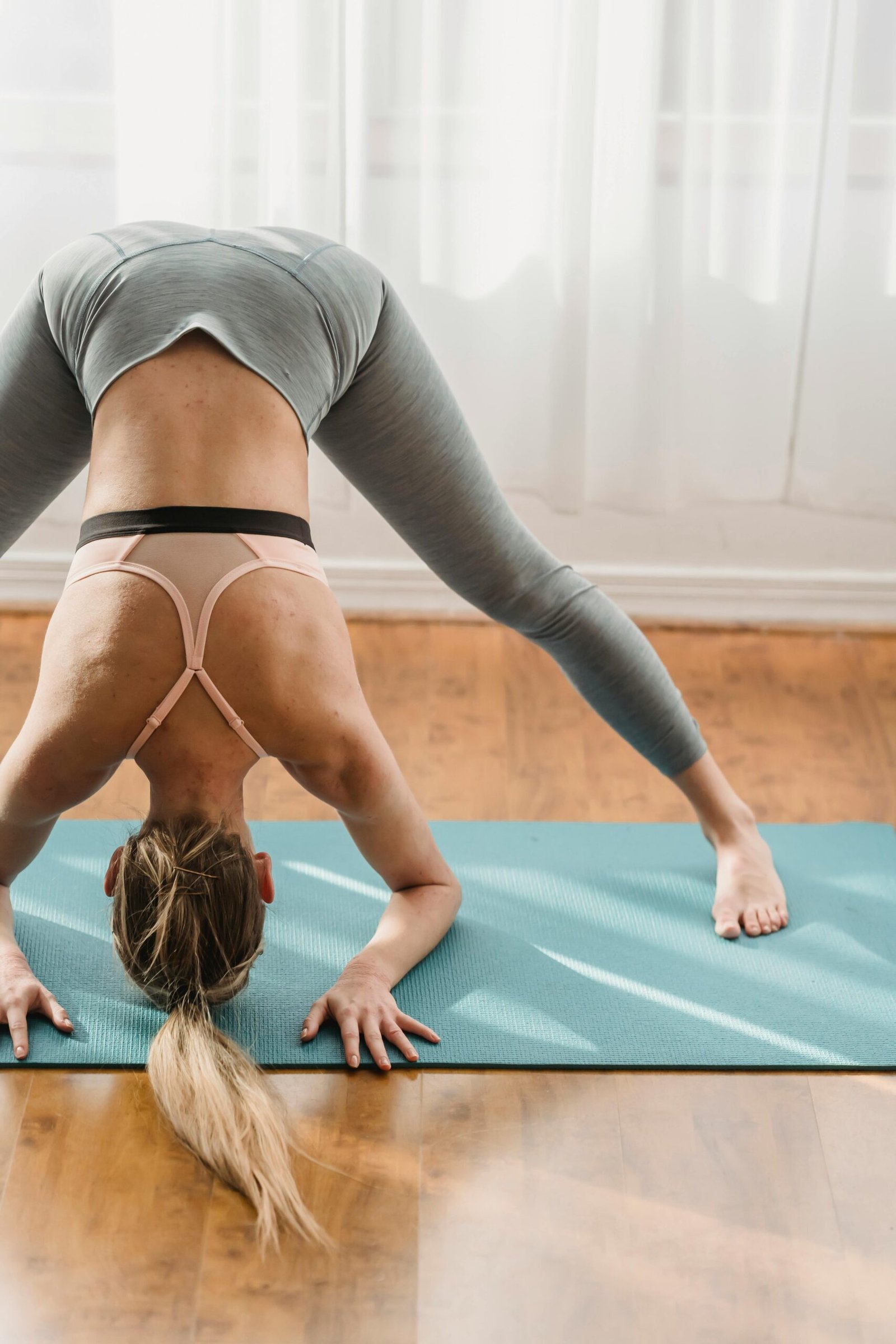 Unrecognizable sportive female in activewear practicing headstand preparation posture while standing on mat during yoga training in light room at home